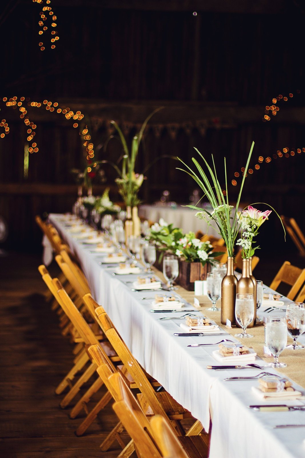 A long reception table set with white linens, golden chairs, and delicate floral arrangements
